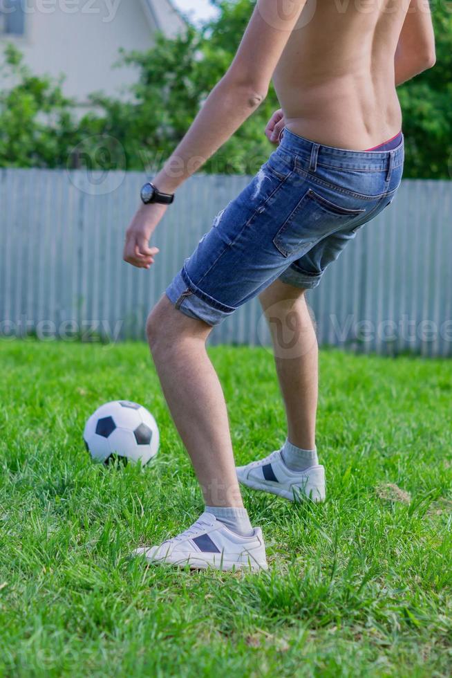 giovane in jeans denim e scarpe da ginnastica bianche che giocano a pallone da calcio all'aperto. giocatore di football amatoriale coniare la palla foto