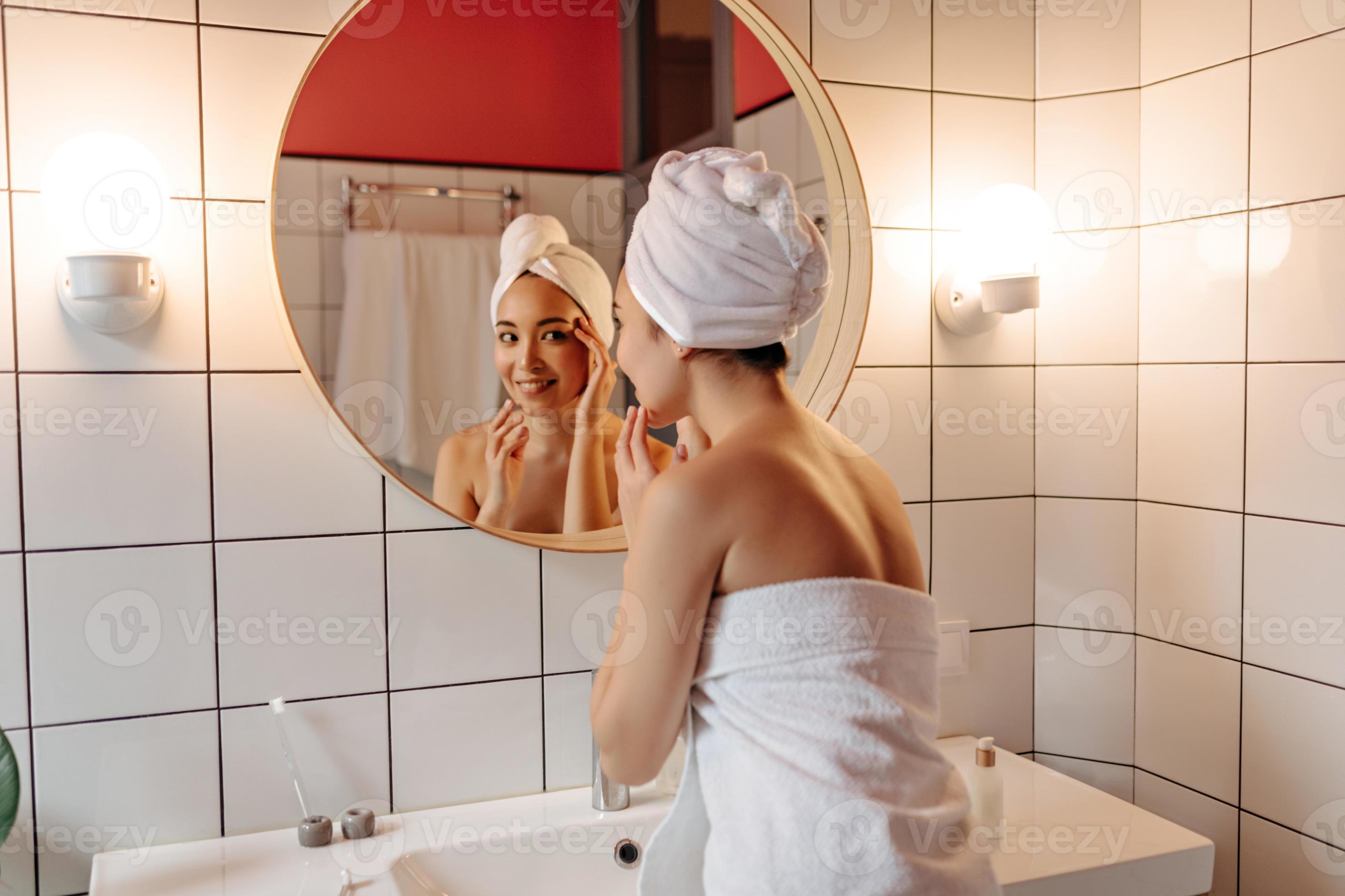 donna nel grande umore fa mattina routine nel bagno. ragazza nel asciugamano  dopo doccia sembra nel specchio 12905952 Stock Photo su Vecteezy