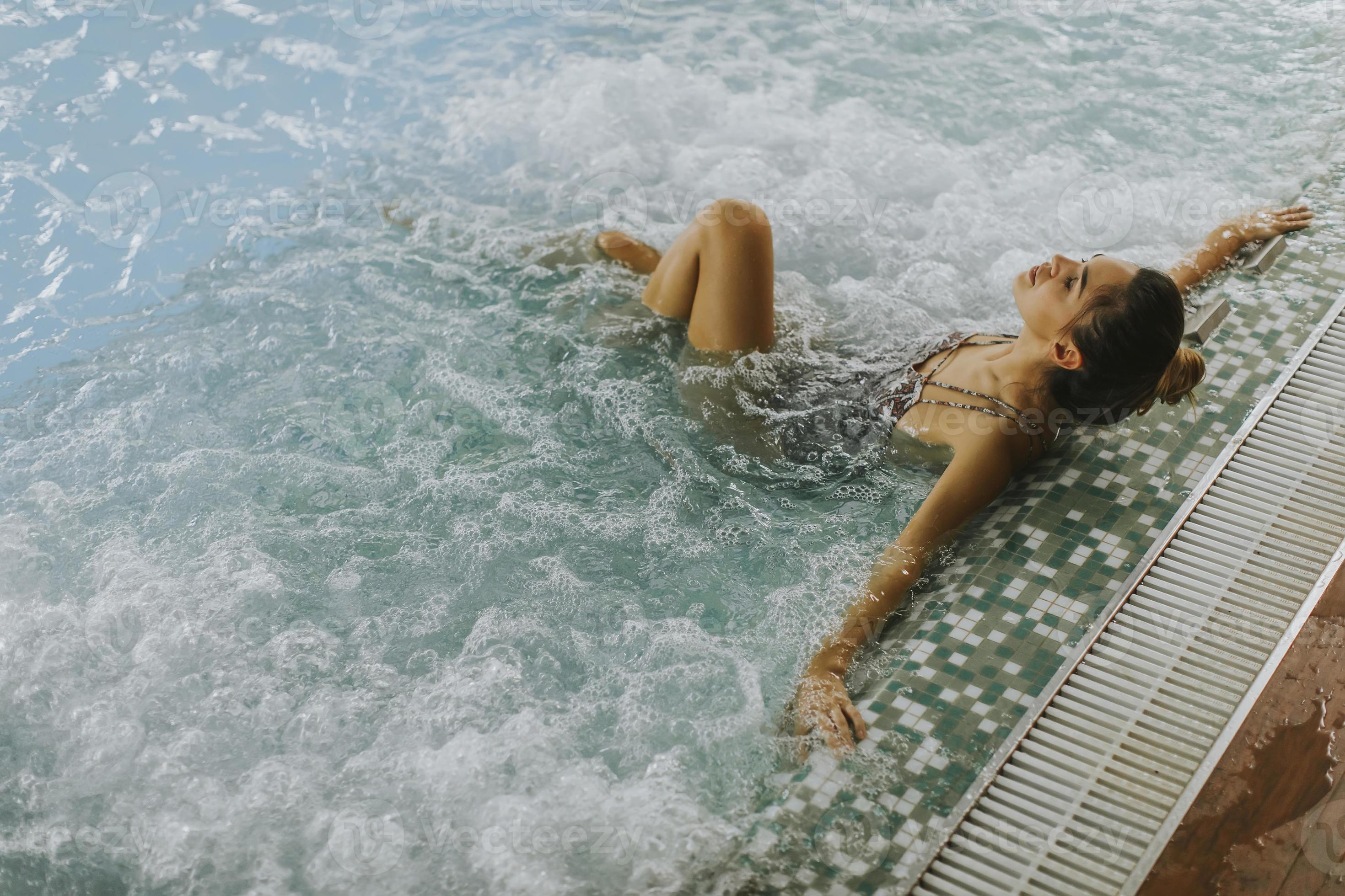 giovane donna che si distende nella vasca idromassaggio a bordo piscina foto