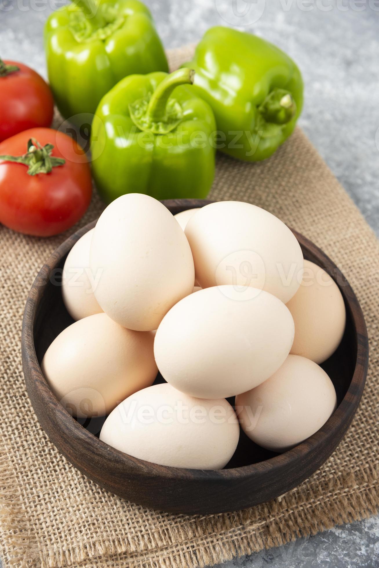 ciotola di legno piena di uova di gallina crude con verdure fresche mature su una tela di sacco foto