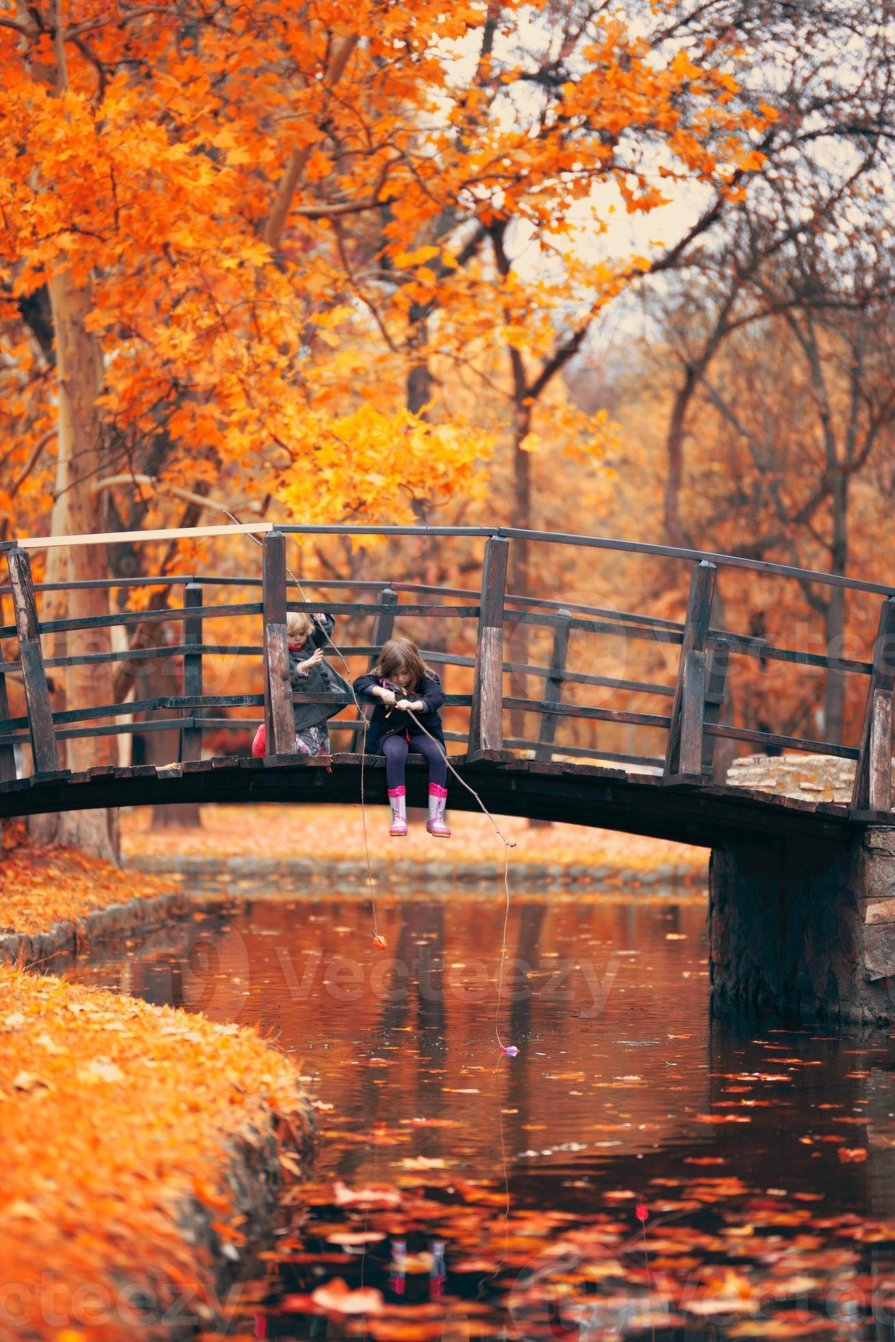 due bambine che si siedono sul ponte di legno e fanno finta che pesca il fondo di autunno foto