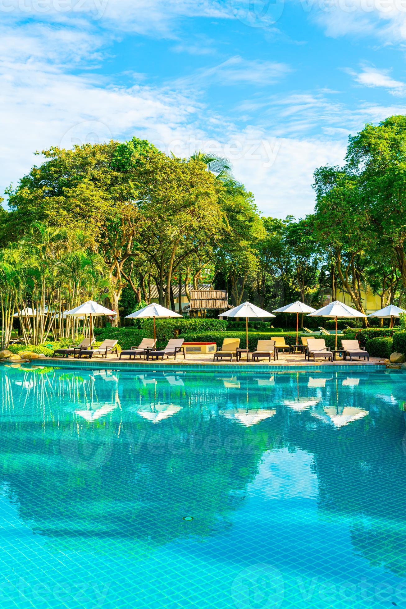 bellissimo ombrellone di lusso e sedia intorno alla piscina all'aperto in hotel e resort con palme da cocco su cielo blu foto
