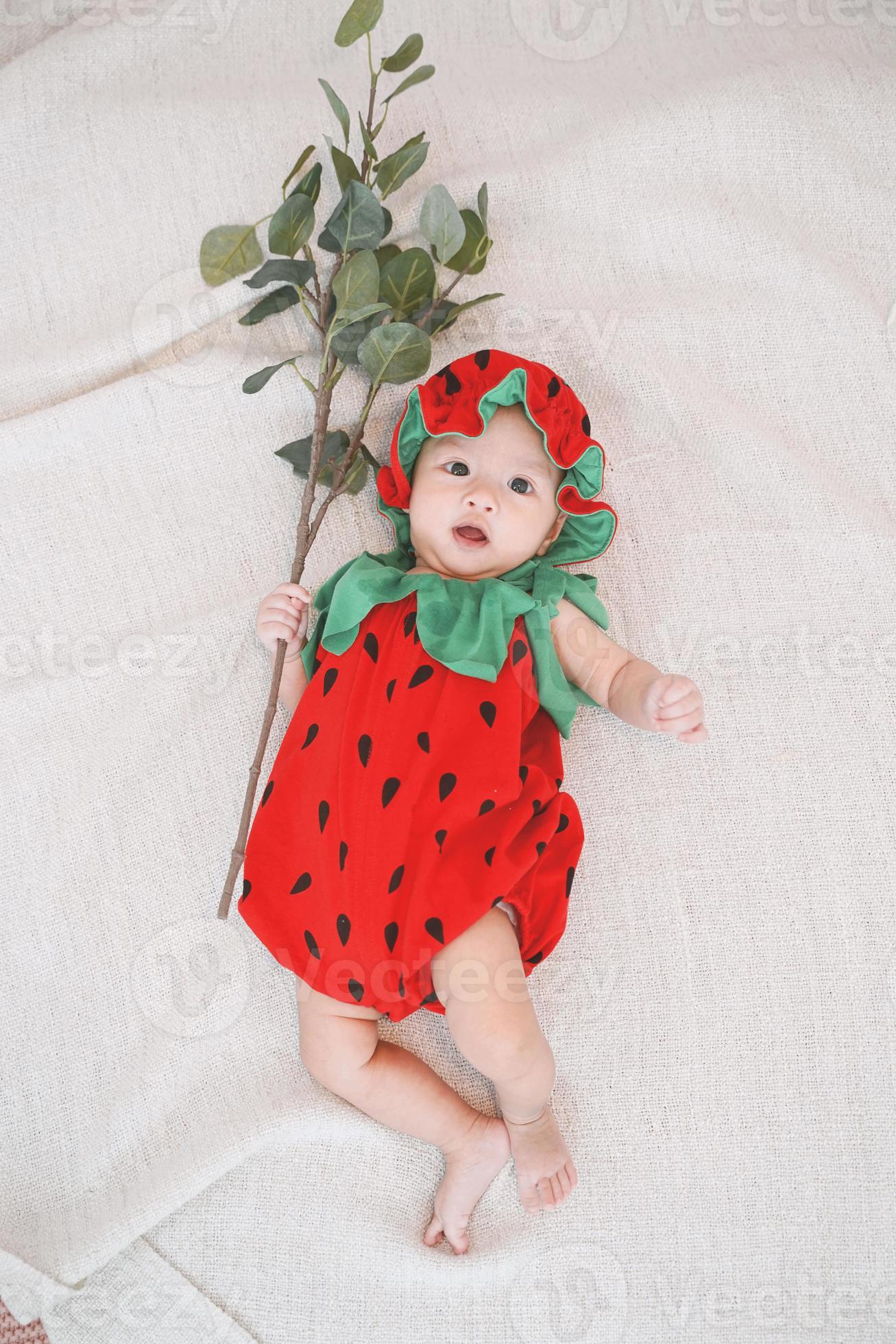 la neonata sveglia indossa un costume da fragola e giace sul letto e tiene  in mano un ramo. vista dall'alto. 2778564 Stock Photo su Vecteezy