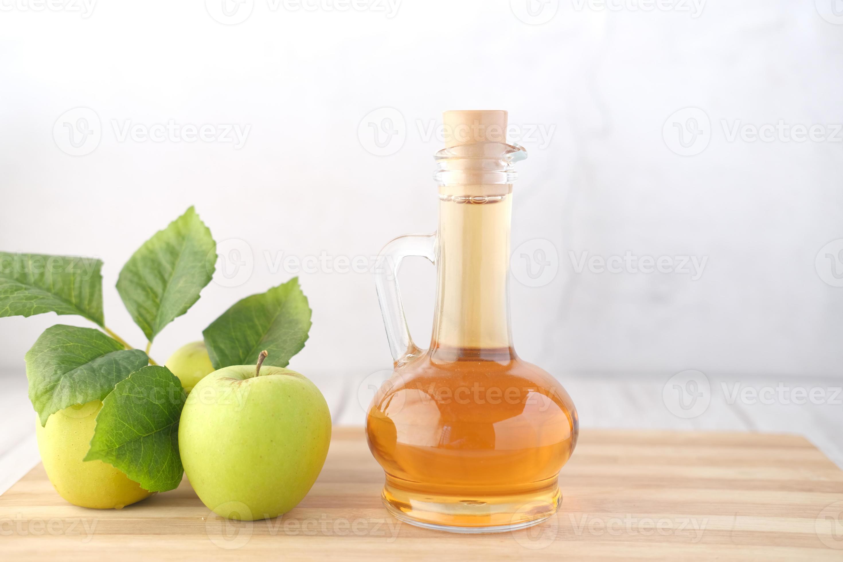 aceto di mele in bottiglia di vetro con mela verde fresca sul tavolo foto