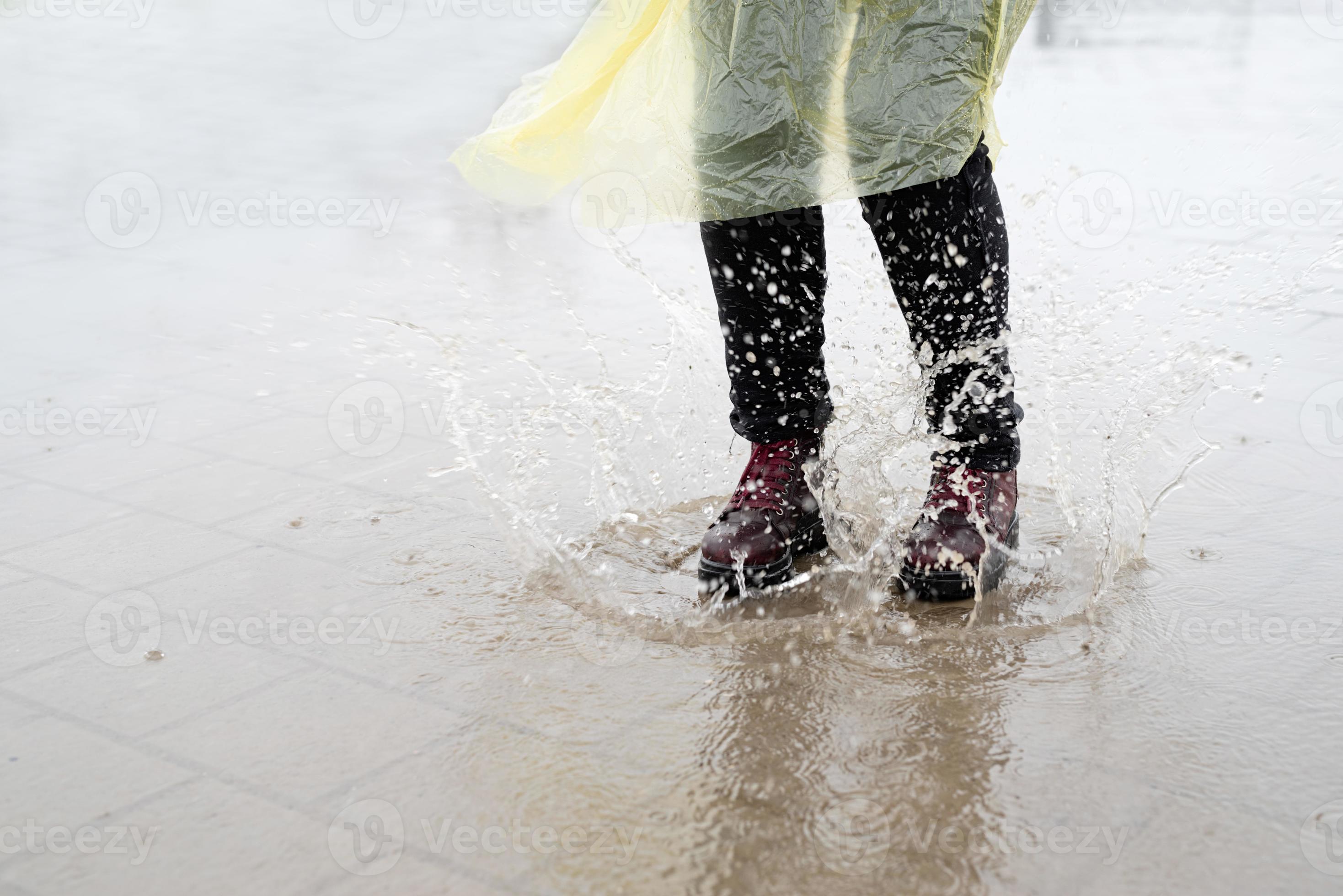 donna che gioca sotto la pioggia, salta nelle pozzanghere con schizzi foto