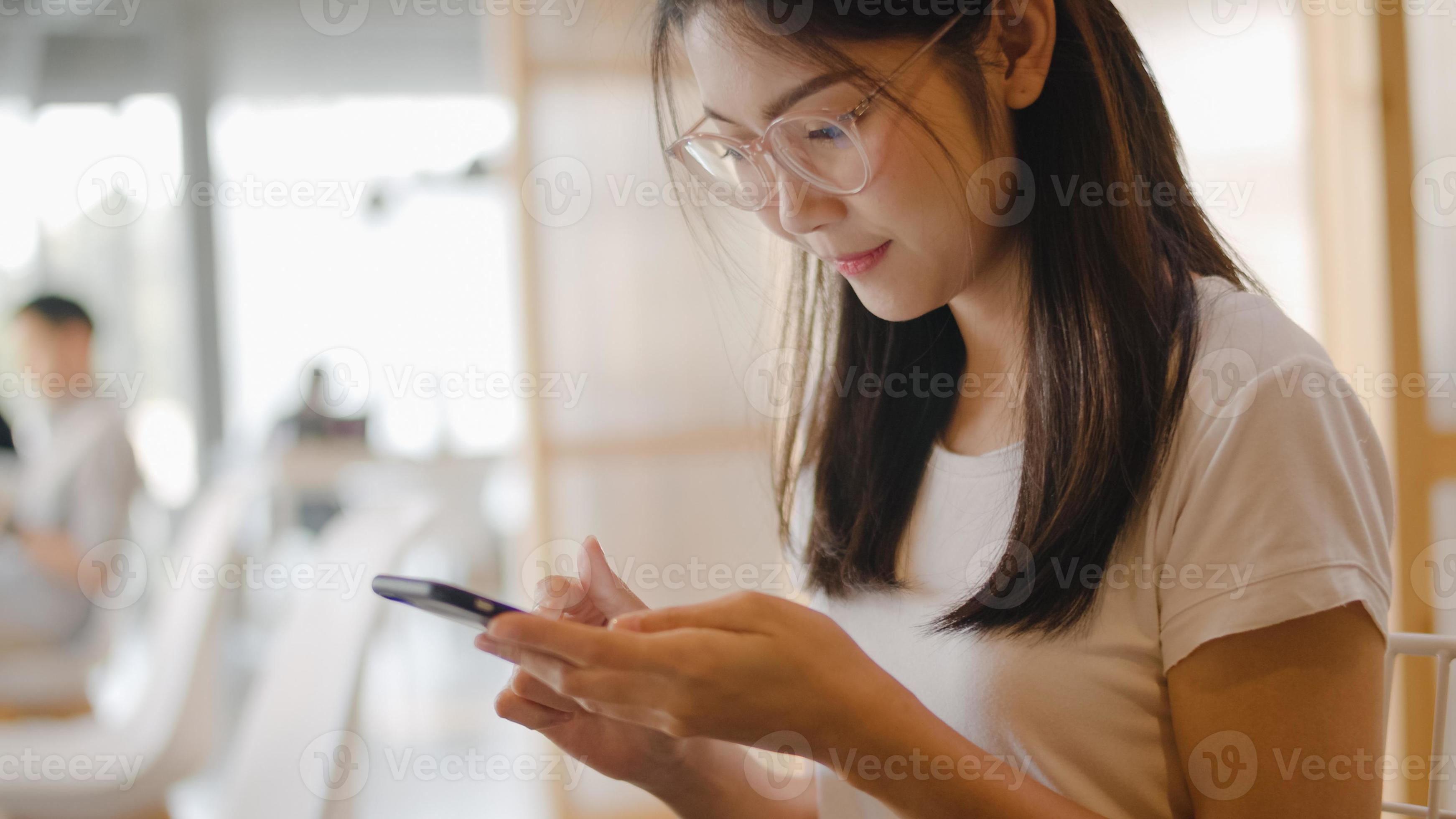 donne asiatiche freelance che utilizzano il telefono cellulare in ufficio. giovane ragazza asiatica giapponese che utilizza smartphone controllando i social media su Internet sul tavolo al concetto di posto di lavoro. foto