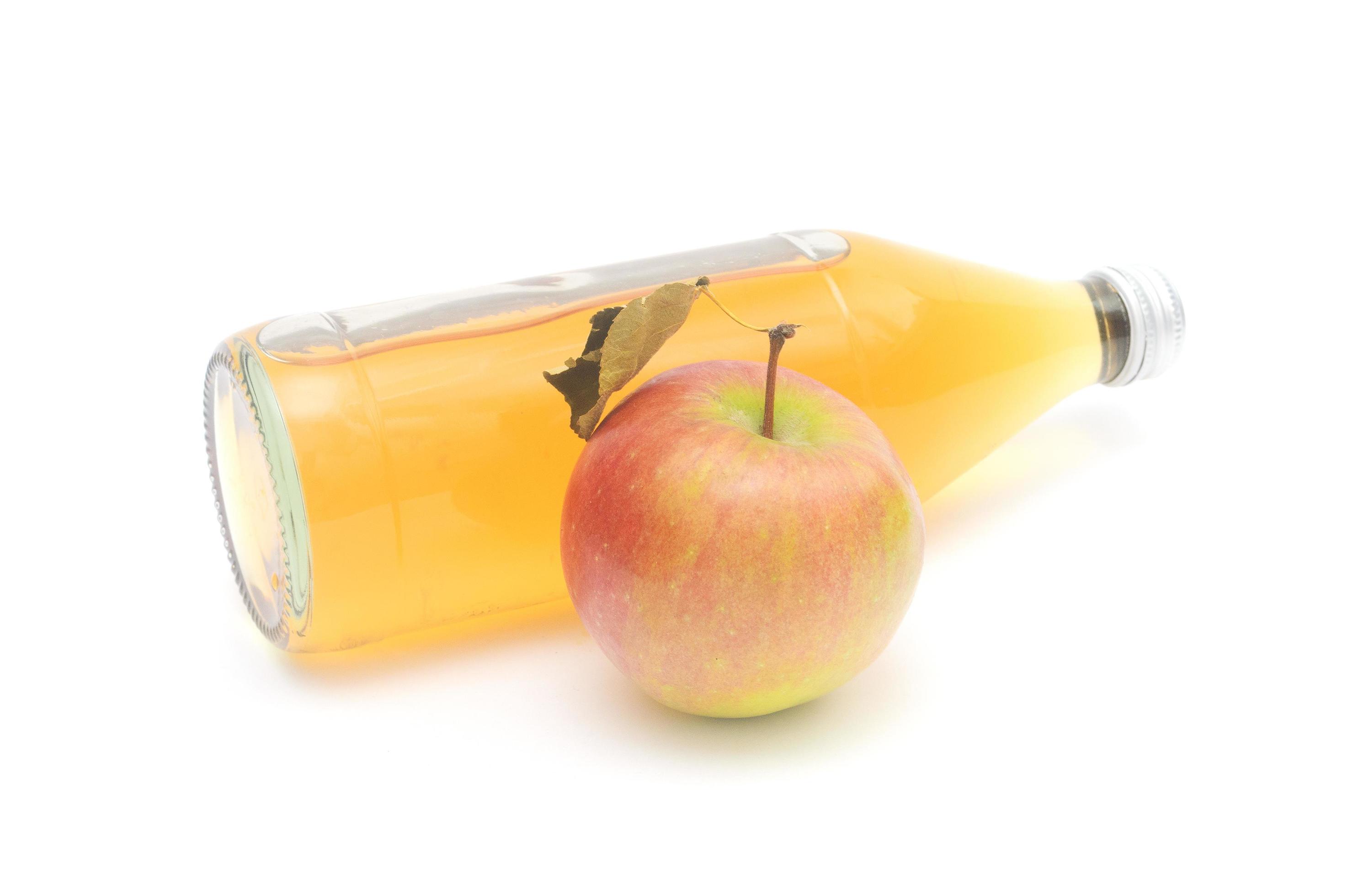 una mela intera con foglia e una bottiglia sdraiata di aceto di mele isolato su sfondo bianco. foto