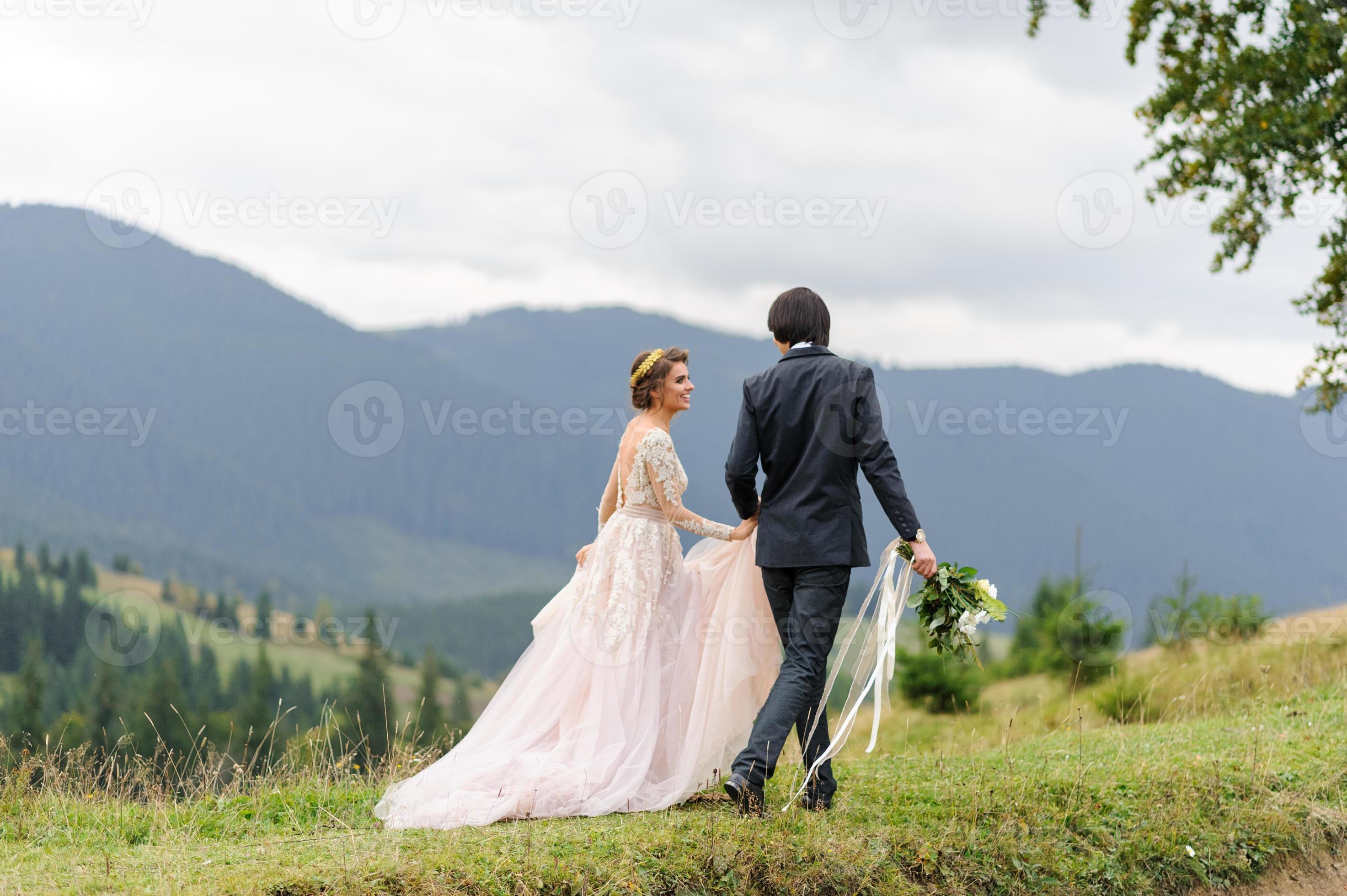 gli sposi camminano per mano sullo sfondo delle montagne. foto del matrimonio.