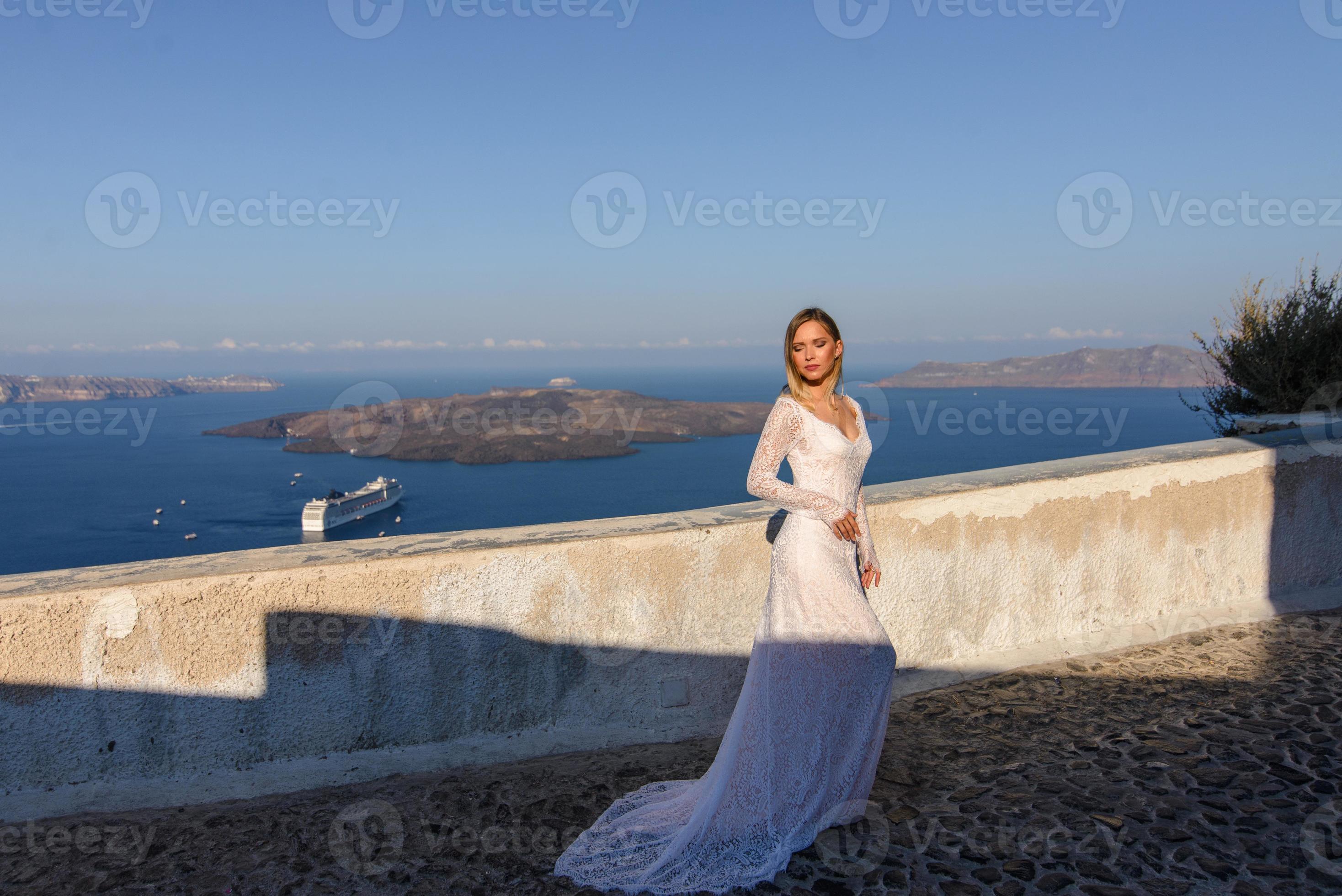 bella sposa in abito bianco in posa sullo sfondo del mar mediterraneo a thira, santorini. foto