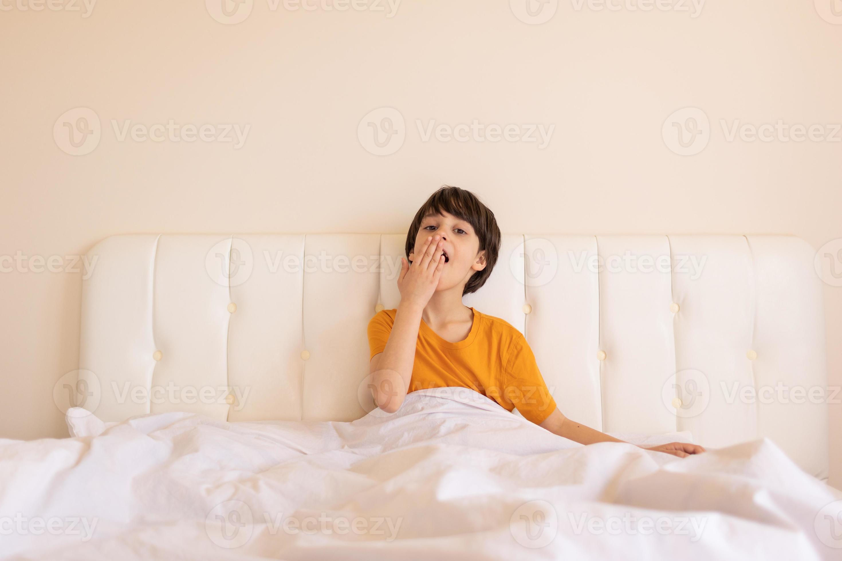 il bambino si sveglia e si siede sul letto, il ragazzo sbadiglia 7139062  Stock Photo su Vecteezy