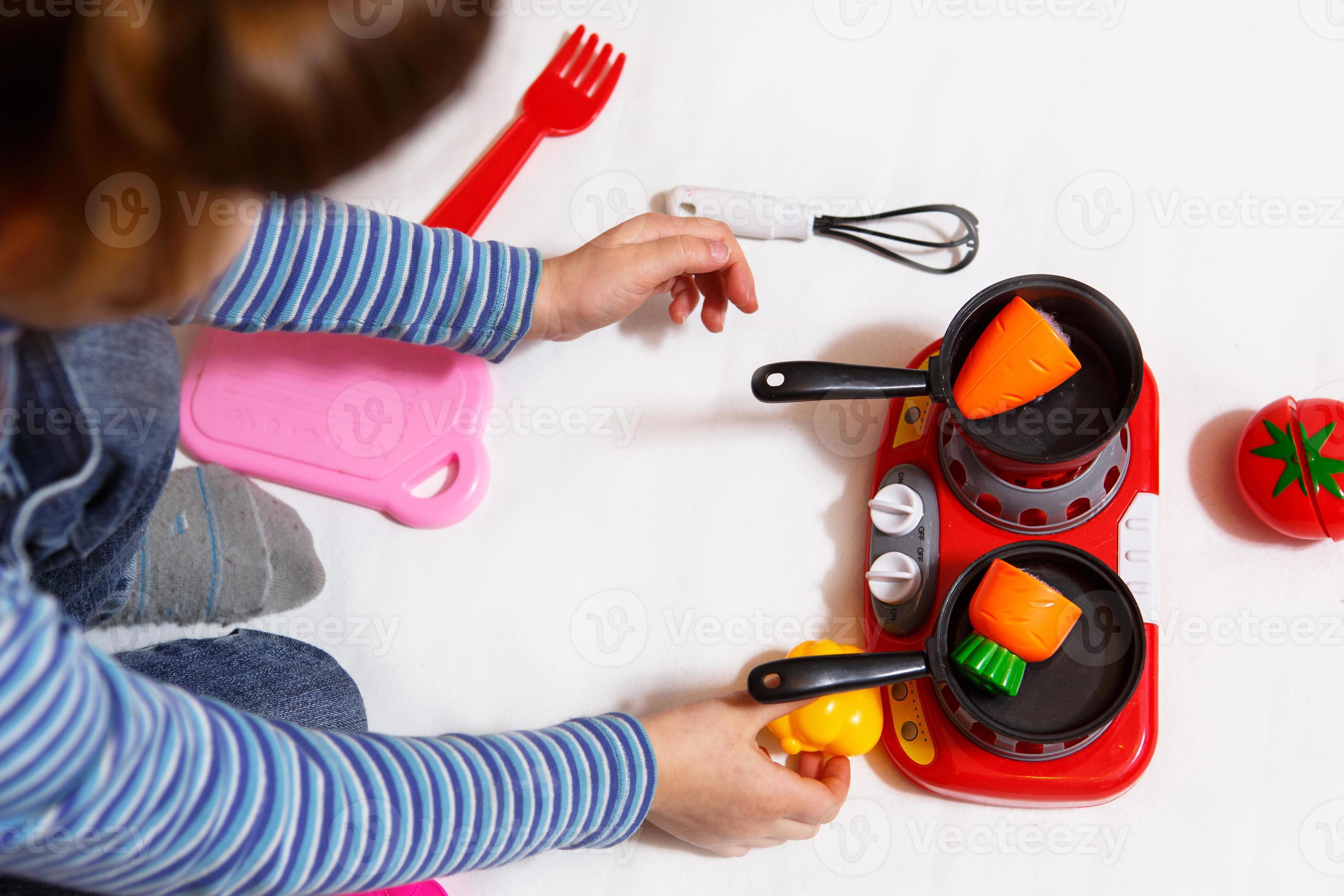 il bambino gioca con frutta e verdura di plastica a fette con il velcro,  cuoce il cibo su un fornello giocattolo in una ciotola. cucina per bambini,  una ragazza impara a cucinare.