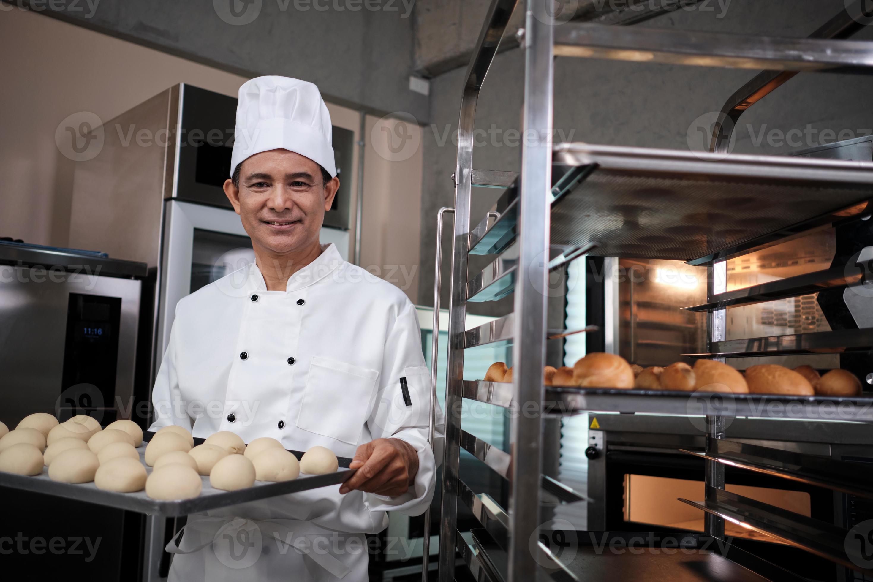 chef maschio asiatico senior in uniforme bianca da cuoco e cappello che  mostra vassoio di pane fresco e gustoso con un sorriso, guardando la  fotocamera, felice con i suoi prodotti alimentari da