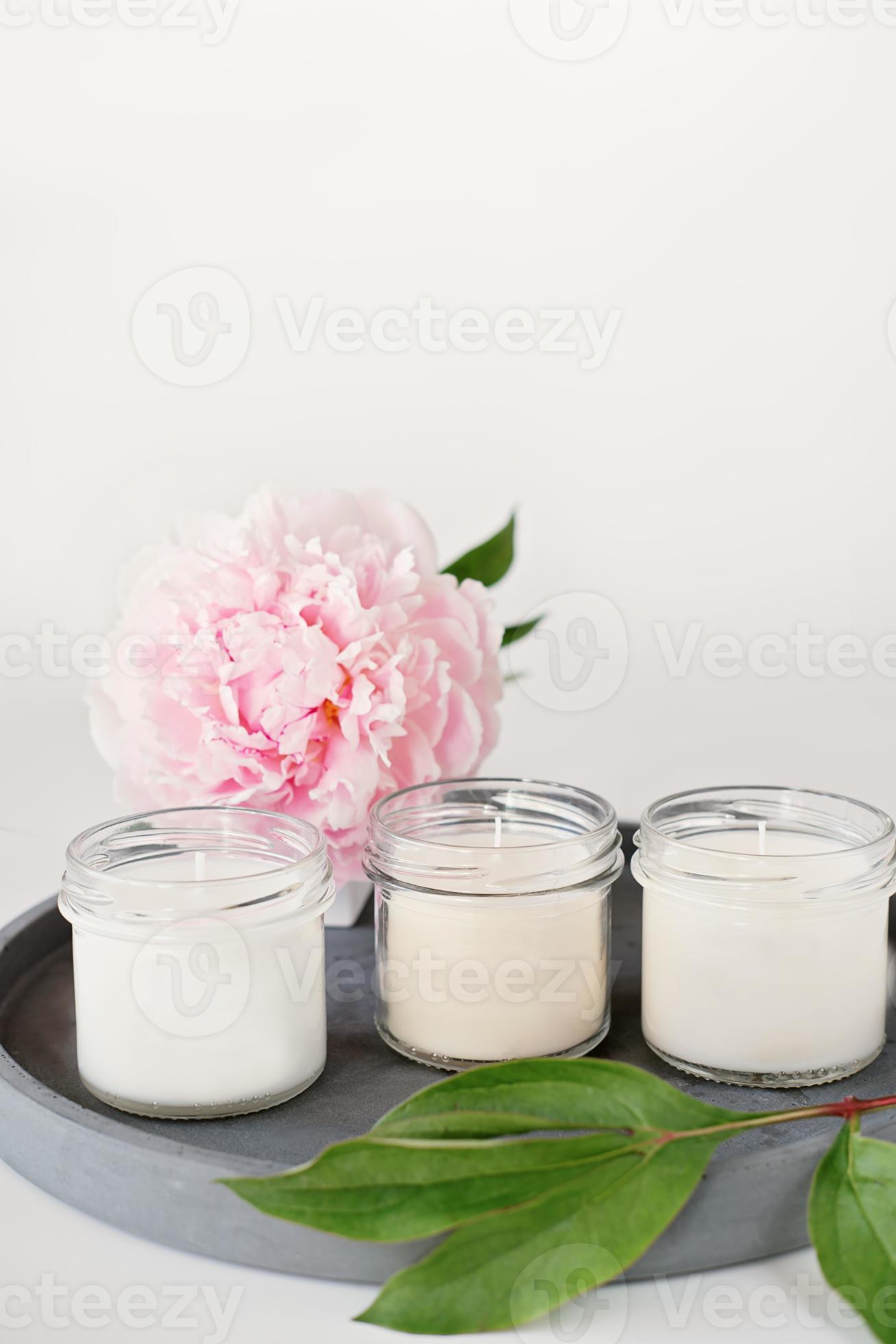 candele profumate bianche su vassoio in cemento e fiore di peonia. Candele  aromatiche di cera di soia in confezione di vetro senza marchio. fragranze  per la casa e casa accogliente 8383747 Stock