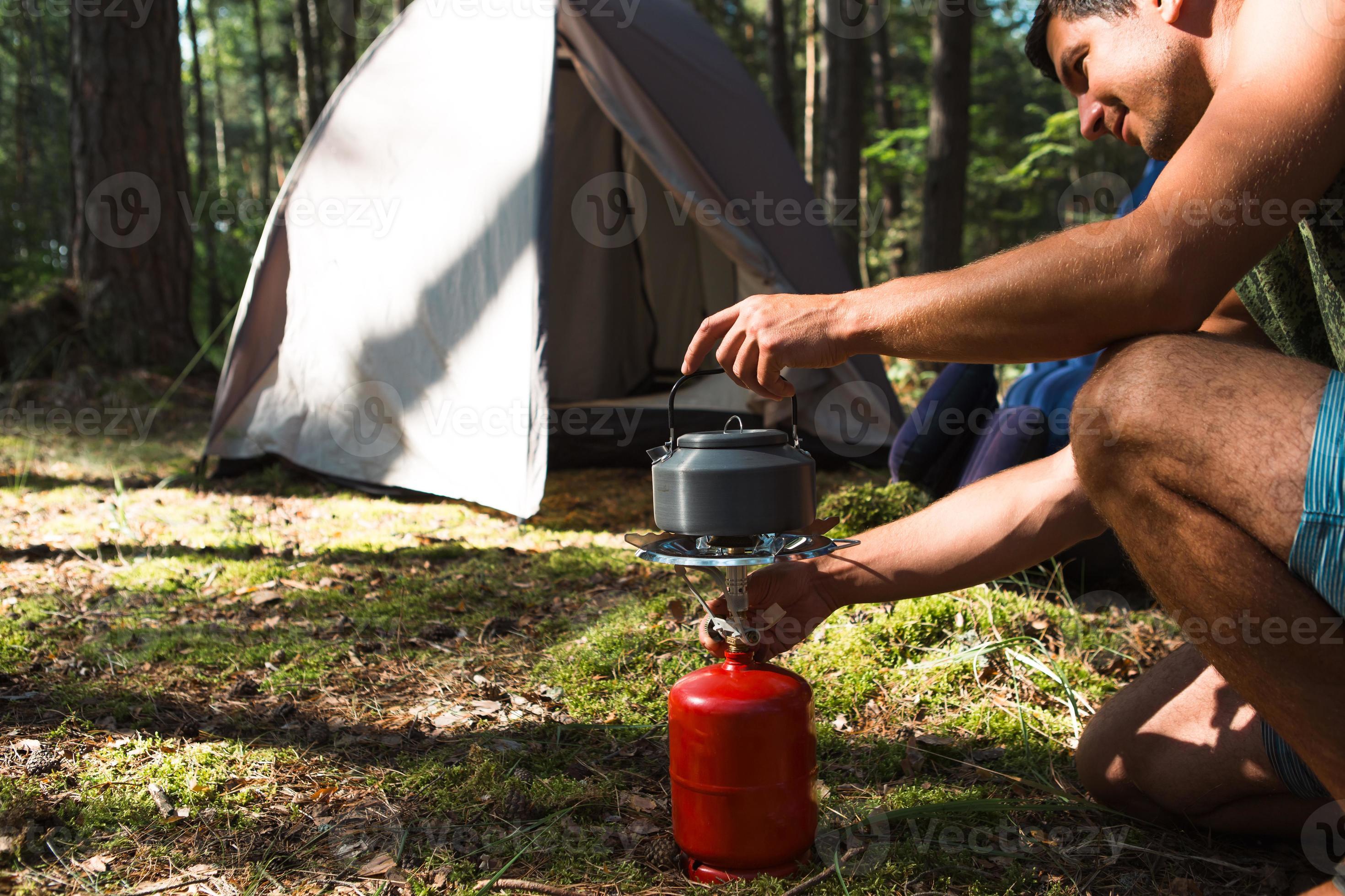 cucinare, riscaldare un bollitore turistico su un bruciatore a gas portatile  con una bombola di gas rossa. campeggio, un uomo prepara la colazione  all'aperto. attività estive all'aperto 8452324 Stock Photo su Vecteezy