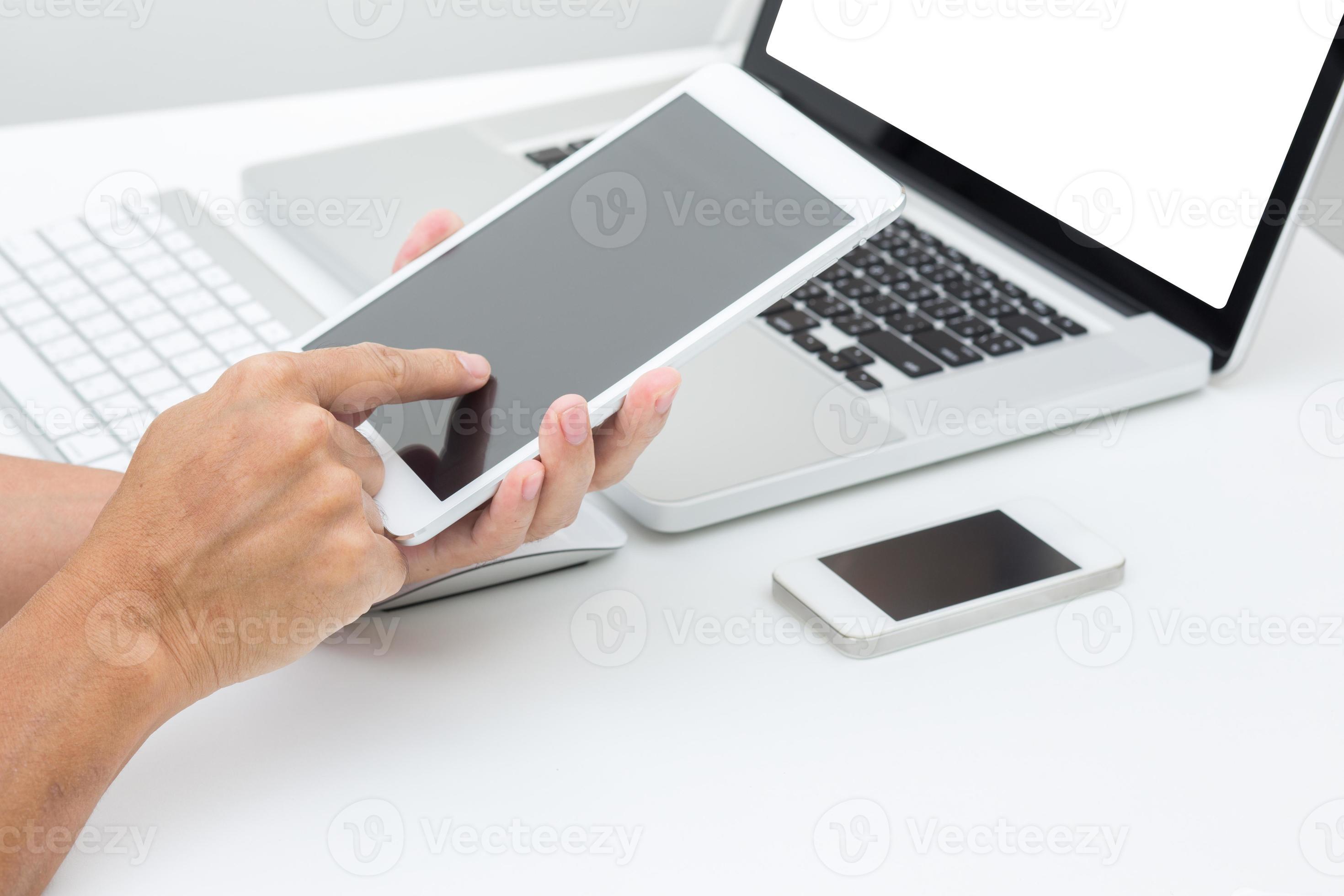 mani dell'uomo che tiene tablet con sfondo di computer portatile foto