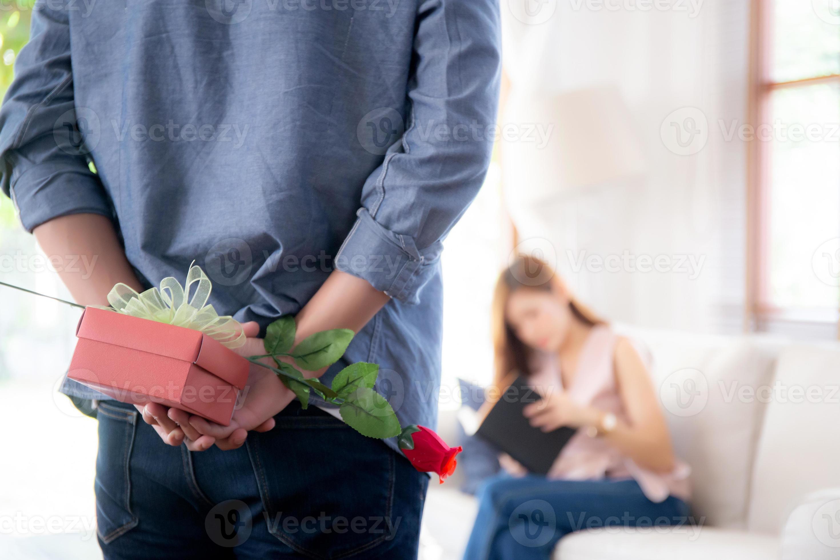 bella giovane coppia asiatica con uomo che nasconde scatola regalo rossa e  fiore rosa per sorpresa a casa, marito e moglie con buon San Valentino o  compleanno, sposati insieme, concetto di amore