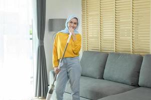 giovane donna musulmana felice che pulisce e aspira il pavimento in soggiorno. foto