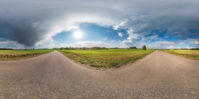 panorama sferico completo senza soluzione di continuità vista a 360 gradi su strada asfaltata senza traffico tra vicoli e campi con fantastiche nuvole in proiezione equidistante equirettangolare, contenuto vr ar foto