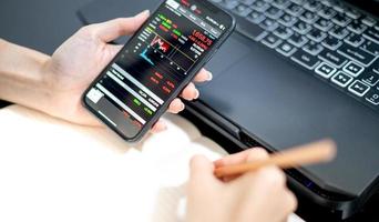 analista broker investitore femminile che tiene in mano uno smartphone analizzando i grafici di trading del mercato azionario indicizzando i dati che controllano il prezzo utilizzando l'applicazione mobile di borsa del mercato azionario. foto