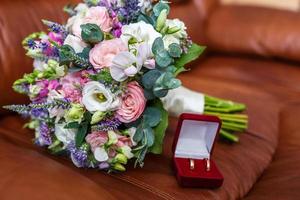 bouquet da sposa luminoso di rose bianche rosa estive e orchidea con fiori di campo viola con fedi nuziali foto