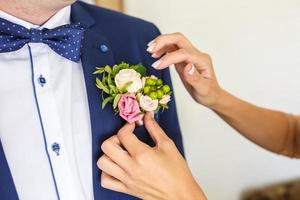 la sposa mette lo sposo su un fiore all'occhiello di rosa e rosa bianca il giorno del matrimonio foto