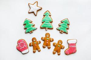 biscotti di pan di zenzero fatti a mano sotto forma di stelle, fiocchi di neve, persone, calzini, personale, guanti, alberi di natale, cuori per le vacanze di natale e capodanno su sfondo di carta bianca foto