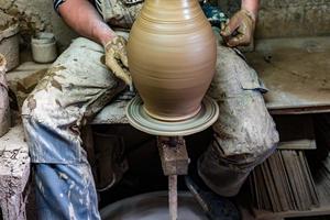 artigiano in abiti sporchi che modella l'argilla nella forma desiderata sul tornio del vasaio. foto