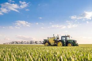 agricoltore che spruzza il campo di grano con l'irroratrice del trattore nella stagione primaverile foto