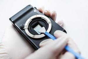 primo piano di mirrorless digital aps-c fotocamera sporca sensore a matrice pulizia e manutenzione con tampone, fotografo pulizia fotocamera su sfondo bianco foto