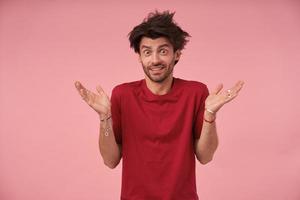 bell'uomo barbuto con capelli selvaggi in abbigliamento casual in piedi su sfondo rosa con le mani alzate, guardando la fotocamera con la faccia sorpresa, contraendo la fronte e alzando le sopracciglia con gli occhi spalancati foto