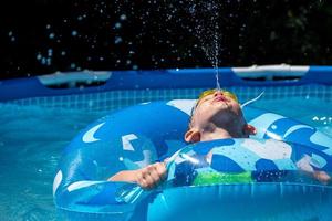 giovane ragazzo che sputava acqua verso l'alto nella piscina del cortile foto