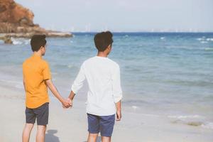 omosessuale giovane coppia asiatica in piedi insieme sulla spiaggia in estate, asia gay che si tiene per mano andando in mare per il tempo libero e rilassarsi con romantico e felice in vacanza al mare, lgbt con concetto legale. foto