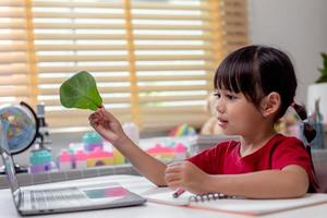 tempo di apprendimento. la scolaretta interessata con le cuffie si siede a casa e guarda la video lezione di istruzione. curiosa ragazza in età scolare pensa alla domanda dell'insegnante seleziona la risposta corretta sullo schermo del laptop foto