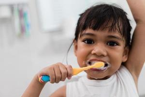 piccola neonata sveglia che si pulisce i denti con uno spazzolino da denti in bagno foto