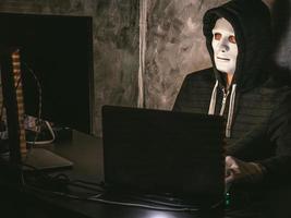 hacker di computer - uomo in maglietta con cappuccio con maschera che ruba i dati dal laptop foto