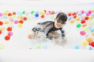 ragazzo che gioca con la palla colorata nel giocattolo della piccola piscina - ragazzo felice nel concetto del giocattolo della piscina d'acqua foto