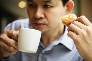 uomo assonnato che beve caffè con pane - persone con concetto di bevanda al caffè con caffeina foto