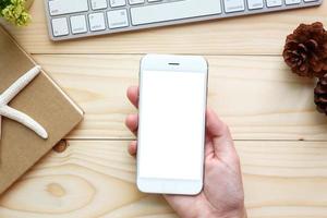 mani della donna che tengono lo schermo vuoto dello smartphone sul lavoro di scrivania in legno. foto