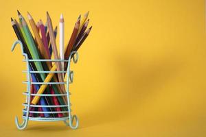 un sacco di matite colorate da disegno in un vetro verde su sfondo giallo, spazio per la copia. foto