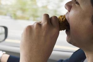 uomo d'affari che guida l'auto mentre mangia pericolosamente pollo fritto foto