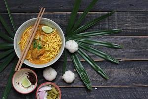 ricetta khao soi, khao soi, khao soi kai, thai noodles khao soi, pollo al curry con condimento servito su tavola di legno foto