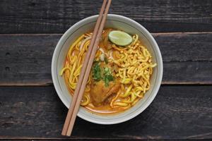 ricetta khao soi, khao soi, khao soi kai, thai noodles khao soi, pollo al curry con condimento servito su tavola di legno foto