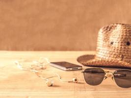 occhiali da sole, cappello, smartphone e auricolari sul tavolo di legno foto