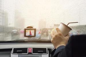 uomo che guida l'auto usando il navigatore e tenendo una tazza di caffè in una giornata piovosa foto