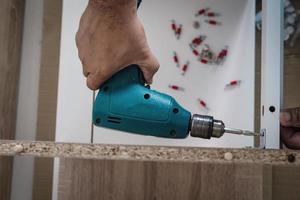 l'uomo sta lavorando con l'assemblaggio di mobili utilizzando un cacciavite elettrico nell'installazione di una nuova casa - lavoro tecnico in loco utilizzando il concetto di utensili manuali foto