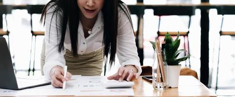 Close up imprenditrice o ragioniere mano che tiene la penna lavorando sulla calcolatrice per calcolare i dati aziendali, documenti contabili e computer portatile in ufficio, concetto di business foto