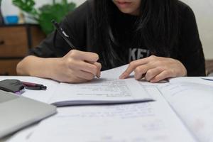 studentessa asiatica sta scrivendo i compiti e leggendo un libro alla scrivania foto