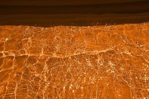 sfocatura sfocata acqua arancione che brilla nel mare. sfondo di dettagli d'acqua increspata. la superficie dell'acqua nel mare, sullo sfondo dell'oceano. onda d'acqua sotto il fondo di struttura del mare. foto
