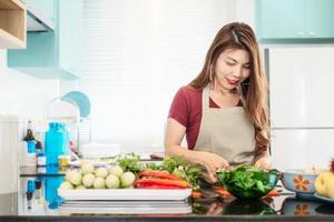 la giovane signora nella cucina moderna e luminosa prepara il cibo con verdure colorate - persone e casa che fanno il concetto di attività di cucina foto