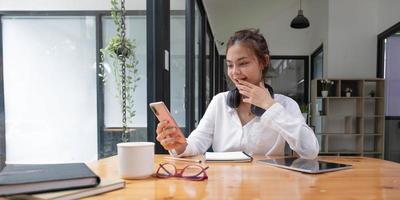 felice giovane ragazza asiatica seduta sul divano a casa tenendo il telefono guardando lo schermo agitando la mano videochiamando amico a distanza online nell'app di chat mobile utilizzando l'applicazione di videochat per smartphone. foto